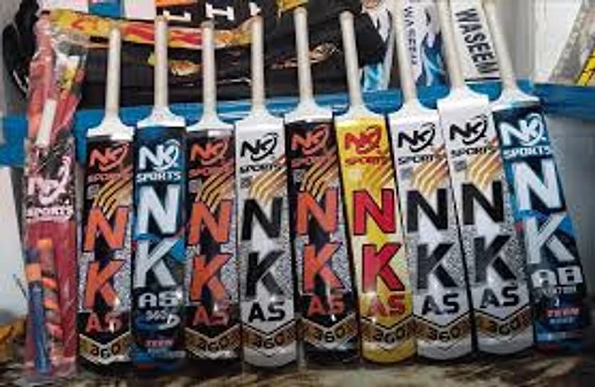 A rack of NK Sports tape ball cricket bats with brightly stickered faces, as stocked in a Pakistani sports shop